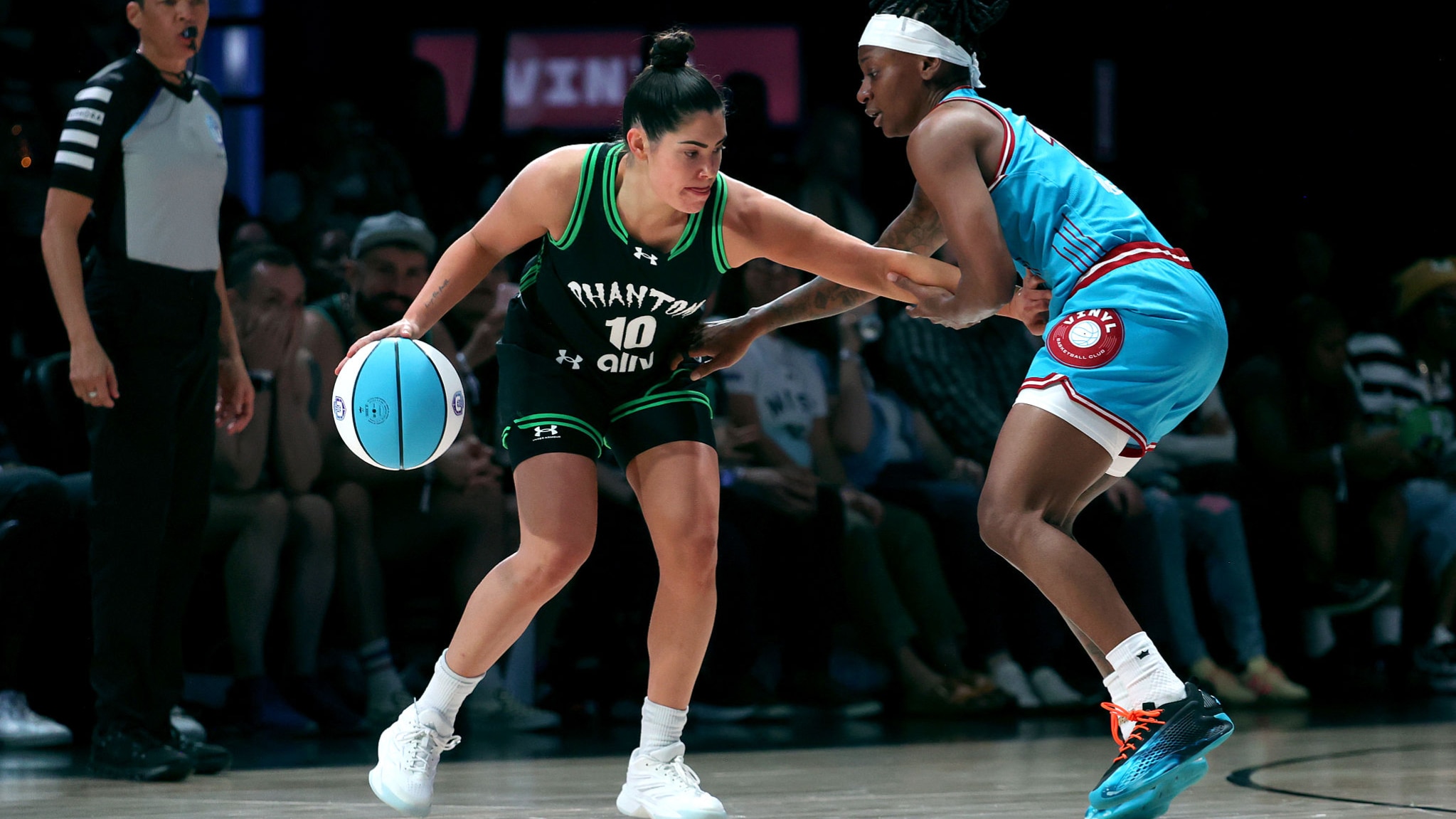 Two athletes intensely competing in a one-on-one basketball game, with one player driving towards the basket while the other defends.